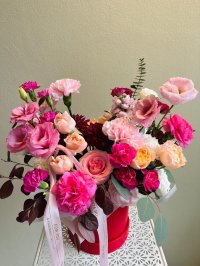A vibrant floral box filled with pink and peach roses, lisianthuses, and carnations.