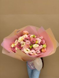 A pastel bouquet of pink, cream, and peach lisianthuses wrapped in blush and champagne paper.