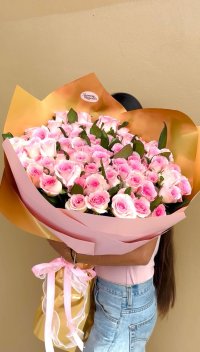 A large bouquet of pink roses wrapped in blush pink and gold paper.