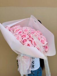 A large bouquet of soft pink roses wrapped in pastel pink paper with delicate love-themed ribbon.