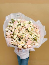 A pastel bouquet of blush pink and cream roses wrapped in soft white paper.