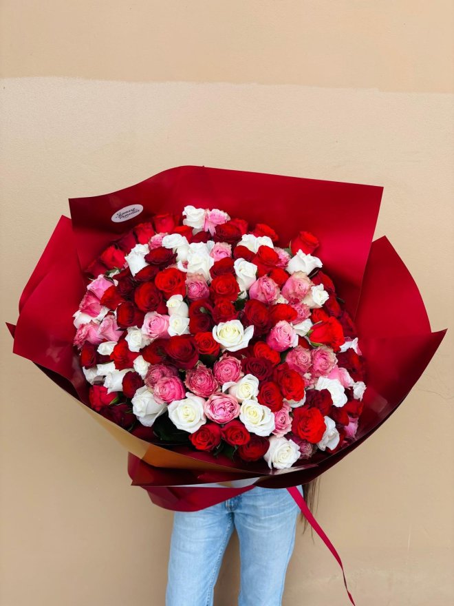 A large bouquet of red, pink, and white roses wrapped in bold red paper.