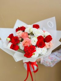 A bouquet with red and pink roses, white lisianthus, carnations, and chrysanthemums tied with red ribbon.