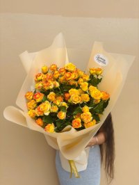 A bouquet of vibrant yellow and orange spray roses wrapped in soft cream paper.
