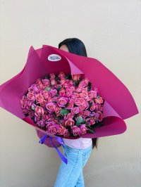 A large bouquet of purple-pink roses wrapped in deep plum paper.
