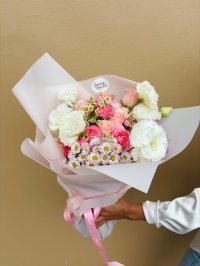 A pastel bouquet of pink and white roses, lisianthuses, carnations, and chrysanthemums wrapped in blush pink paper.