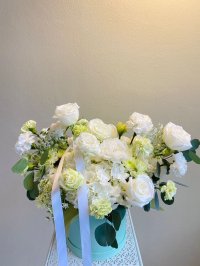 A pastel box arrangement of white roses, hydrangeas, and green-tinted carnations with soft foliage.