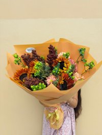 A rustic bouquet of sunflowers, red millet, chrysanthemums, and green berries wrapped in amber paper.