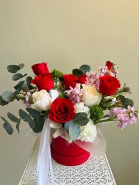 A red floral box with red roses, white carnations, and pink lisianthuses.