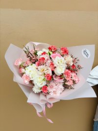 A soft pink and white bouquet featuring roses, lisianthuses, carnations, chrysanthemums, and wax flowers.
