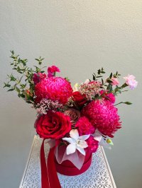 A rich red hatbox bouquet featuring red chrysanthemums, roses, carnations, and white jasmine with ribbon detailing.
