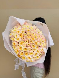 A large bouquet of pastel pink and yellow roses wrapped in soft pink and white paper.