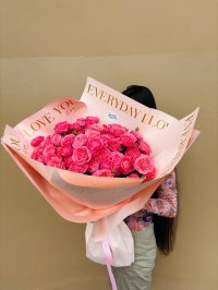 A grand bouquet of vibrant pink roses wrapped in elegant peach paper with gold lettering.