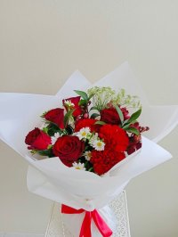 A white-wrapped bouquet with red roses, red carnations, white daisies, and greenery.