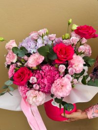 A radiant pink hatbox filled with pink roses, hydrangeas, lisianthuses, and carnations, accented with greenery.