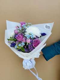 A white-wrapped bouquet with purple roses, white chrysanthemums, blue forget-me-nots, and violet statice flowers.