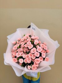 A bouquet of peach-pink spray roses wrapped in soft white paper.