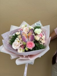 A pastel bouquet featuring pink roses, lisianthuses, and carnations with a decorative butterfly on top.