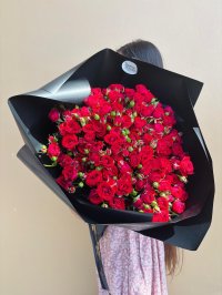 A luxurious bouquet of red spray roses wrapped in matte black paper with black and gold ribbon.