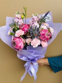 A stunning bouquet featuring pink lotus flowers, pink carnations, and purple veronica, wrapped in lilac paper.
