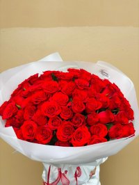 A large bouquet of premium red roses wrapped in white paper with red ribbon.