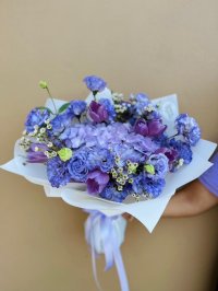 A lavender bouquet with hydrangeas, lisianthus, carnations, tulips, and wax flowers in soft purple and blue tones.