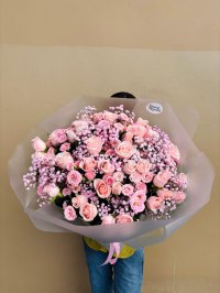 A bouquet of blush pink roses and baby’s breath wrapped in grey paper.