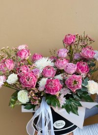 A floral arrangement in a box featuring pink folded lotus flowers, white lisianthus, roses, chrysanthemums, and wax flowers.