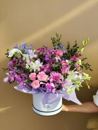 A rich hatbox bouquet with purple orchids, pink roses, carnations, lisianthuses, white blooms, and blue agapanthus.