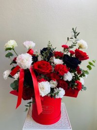 Red, white, and black floral arrangement with roses, carnations, and lisianthus in a red hatbox with red satin ribbon