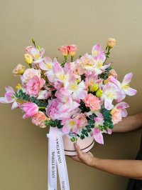 A pastel box filled with pink tulips, carnations, lisianthus, eucalyptus, and a luxurious blush peony at its heart.