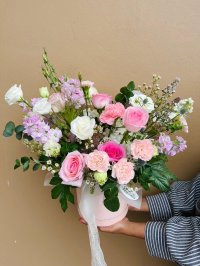 A pastel hatbox arrangement featuring pink roses, carnations, lisianthuses, and wax flowers.