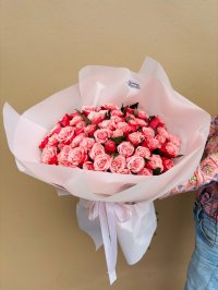 A large bouquet of pink and red roses wrapped in blush paper with white ribbon.