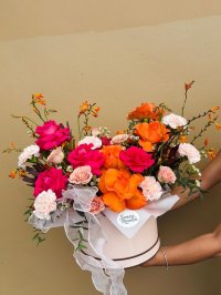 A floral box featuring orange and hot pink roses, peach carnations, and orange accent flowers with white ribbon.