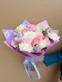 A pastel bouquet with white and pink roses, carnations, lilac stock, and fillers, wrapped in soft lavender and pink paper.