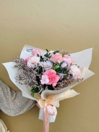 A pastel bouquet featuring pink roses, carnations, and dry flowers wrapped in soft cream paper.