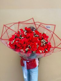 A grand bouquet of red roses accented with baby’s breath, wrapped in red and clear paper.