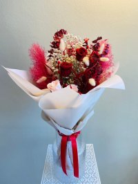 A preserved flower bouquet with red roses, pink pampas, baby's breath, and bunny tails in cream wrapping.