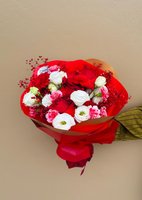 Daria bouquet with white lisianthus, red and pink carnations, and burgundy baby's breath wrapped in red paper against neutral background