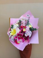 A vibrant pink bouquet featuring lilies, chrysanthemums, carnations, and mixed pastel blooms wrapped in pink paper.