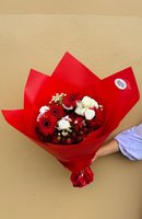 A bouquet of red gerberas, crimson flowers, and white roses wrapped in vibrant red paper.
