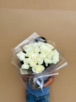 Person holding Angel bouquet of 24 white roses wrapped in clear cellophane with white ribbon against beige wall background