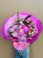 Pink and white Priya bouquet with lisianthus, ranunculus, carnations, wax flowers and purple statice wrapped in bright pink paper, held against bei...