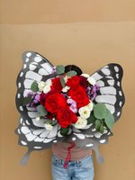 Artistic butterfly-shaped bouquet featuring red roses, white roses, and purple chrysanthemums with eucalyptus leaves, held against a beige backgrou...