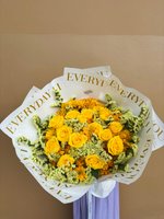 A bouquet of yellow roses and daisies wrapped in white and gold paper, symbolizing remembrance and sympathy.