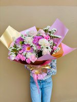 Pink flower bouquet with dahlias, carnations, and statice wrapped in pink and gold paper.