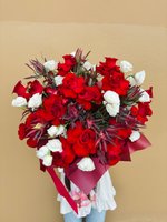Bouquet of red roses and white lisianthus with dark greenery, wrapped in deep red paper.