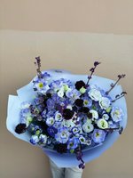 Violet and white lisianthus bouquet with deep berry accents wrapped in pale blue paper.