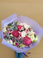 Bouquet of pink, magenta, and white chrysanthemums, roses, and lisianthus with dusty miller foliage, wrapped in lavender paper.