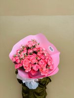 Catherine bouquet featuring 9 pink spray roses wrapped in pink paper with white ribbon, held against a neutral background